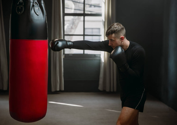 A young athletic man is hitting a boxing bag. Boxer practicing punches in the ring. The athlete strikes with a punching bag. 4k video - Photo, Image