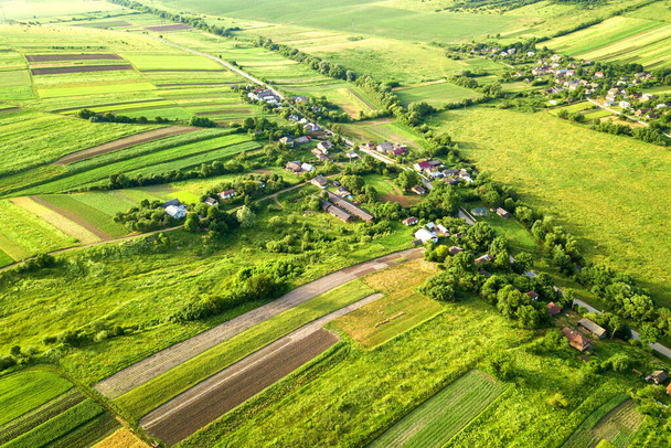 Légi kilátás egy kis falu nyerni sok házat és zöld mezőgazdasági területek tavasszal friss növényzet után vetési szezon egy meleg napos napon. - Fotó, kép
