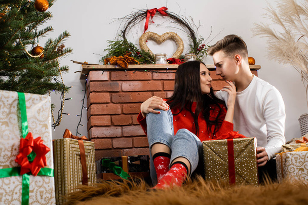 A couple in love are sitting on the floor and flirting. Decorated Christmas tree for Christmas. A unique Christmas atmosphere. - Φωτογραφία, εικόνα