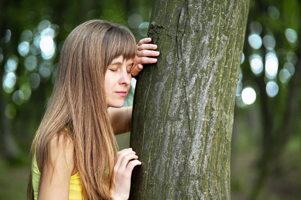 Νεαρή γυναίκα γέρνει στον κορμό των δέντρων στο δάσος του καλοκαιριού. - Φωτογραφία, εικόνα