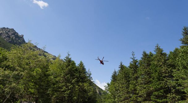 Red helicopter is flying between mountains peak - 写真・画像