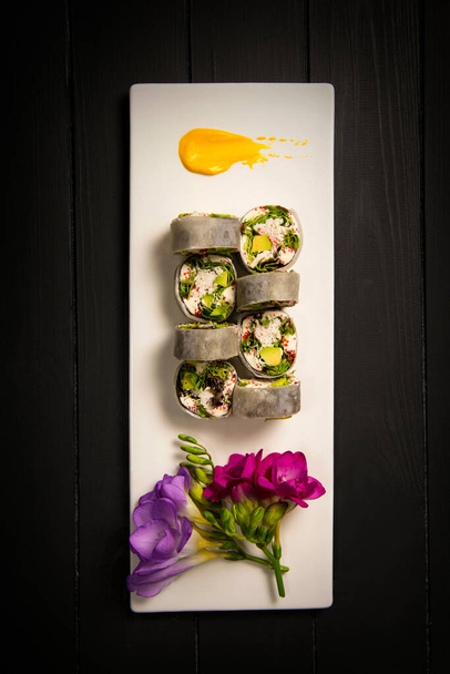 Top näkymä terve japanilainen ei riisiä sushi roll rapu lihaa, avokado kääritty daikon retiisi. Värikkäitä kukkia, keltainen maalaus harja aivohalvaus koristelu valkoinen suorakulmainen levy. Musta tausta - Valokuva, kuva