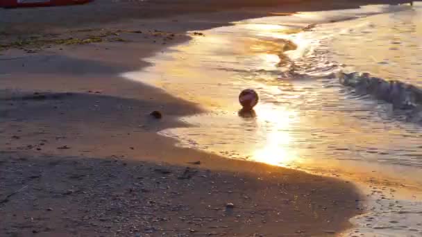 Młody chłopiec gra w piłkę nożną na brzegu o zachodzie słońca. - Materiał filmowy, wideo