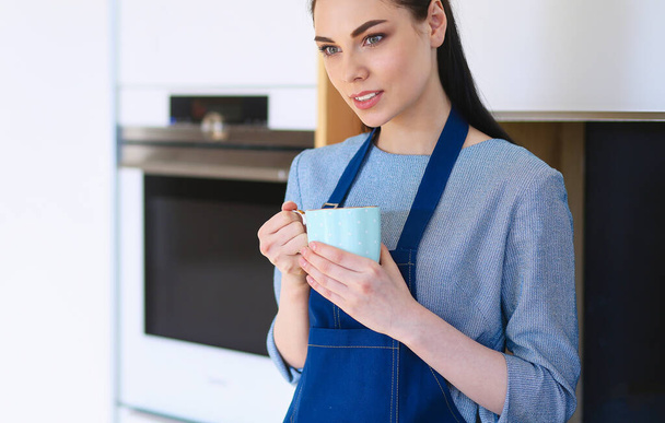 Portrét mladé ženy s šálkem na pozadí kuchyně interiér - Fotografie, Obrázek