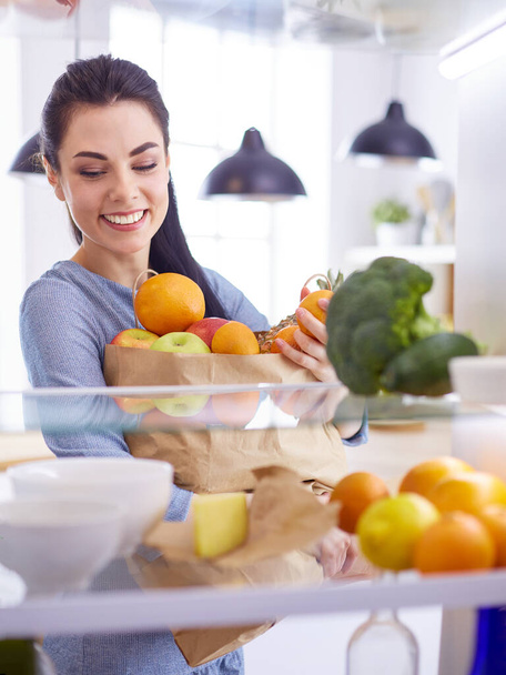 Smiling woman taking a fresh fruit out of the fridge, healthy food concept - 写真・画像