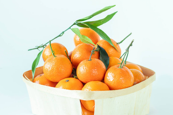 Fresh tangerines with leaves, stands close to a wood basket with white background. Selective focus. - Photo, Image