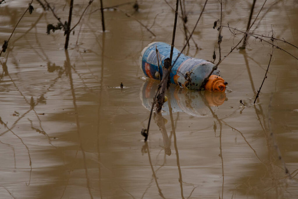 Welland-joessa kelluva muovipullo, joka on ruskea mudassa ja väreilee hieman kevyessä tuulessa.  - Valokuva, kuva