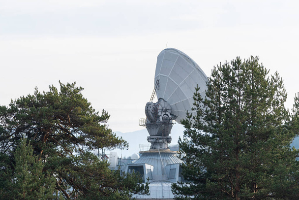 Büyük uydu antenleri yeşil çam ağacı ormanlarında gizlenmiş. Parlak mavi arka planda iletişim merkezi. - Fotoğraf, Görsel