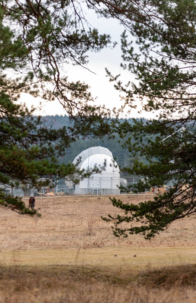 Велика антена супутникової тарілки, захована в зеленому сосновому лісовому центрі зв'язку на фоні лісу
 - Фото, зображення
