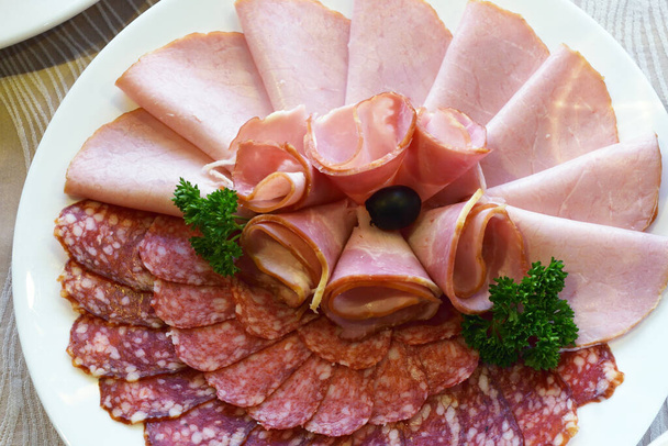 sliced cold snacks in the form of sausages and smoked meats are beautifully laid out on a festive dish - Zdjęcie, obraz