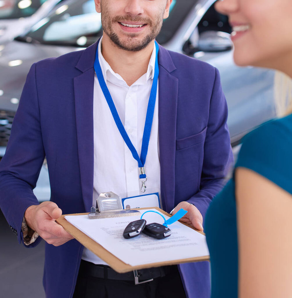 Car salesman sells a car to happy customer in car dealership and hands over the keys - Fotografie, Obrázek