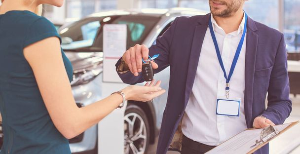 Car salesman sells a car to happy customer in car dealership and hands over the keys - Zdjęcie, obraz