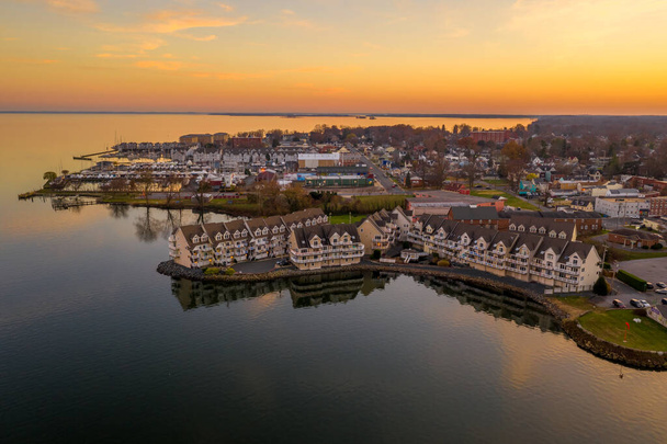 Вид с воздуха на центр города Гавр-де-Грейс в штате Мэриленд с роскошным жилым комплексом на набережной, отражающимся в воде, как солнце рисует небо оранжевым - Фото, изображение