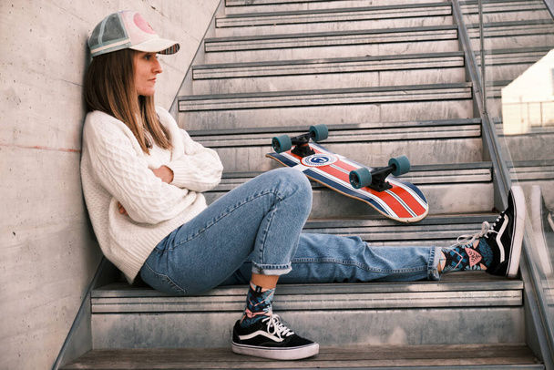 Jonge vrouw met een skateboard zittend op een trap - Foto, afbeelding