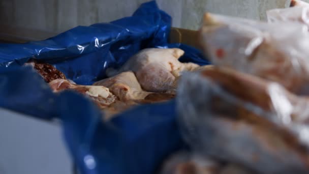 Nahaufnahme eines gebrauchten Handschuhs, der auf eine Schachtel mit gefrorenen Hühnerkeulen geworfen wird. Verpackungs- und Tiefkühlprozess für Hühnerfleisch zur weiteren Verwendung zu Hause. 4K-Video - Filmmaterial, Video