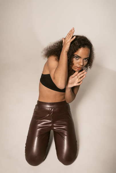 A top view of a frightened young girl stands pinched, covering herself with her hands in leather pants and black top. Women violence and abused concept. trafficking Concept - Foto, imagen
