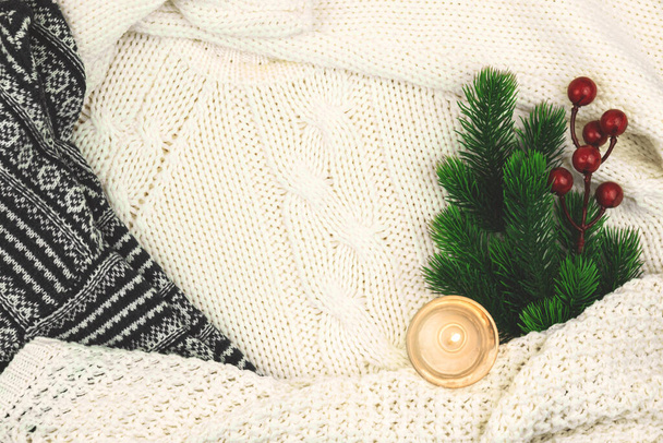 Fondo acogedor de invierno, suéter de lana y punto, rama de abeto con bayas rojas y vela, composición con espacio para copiar - Foto, Imagen