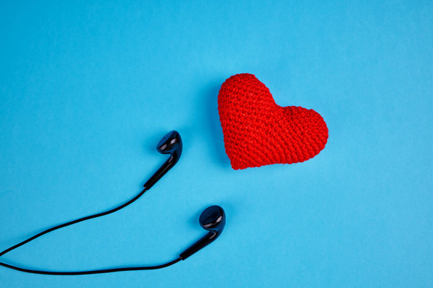 black earphones near red heart over blue background with copy space. love to music rhythm concept - Photo, Image