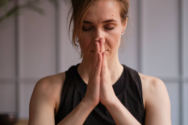 Женщина средних лет медитирует с закрытыми глазами, практикуя йогу руками в молитвенном положении. - Фото, изображение