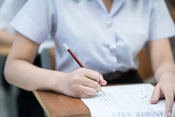 Close up of young university students concentrate on doing examination in classroom. Girl student writes on the examinations answer paper in the classroom. - Photo, Image