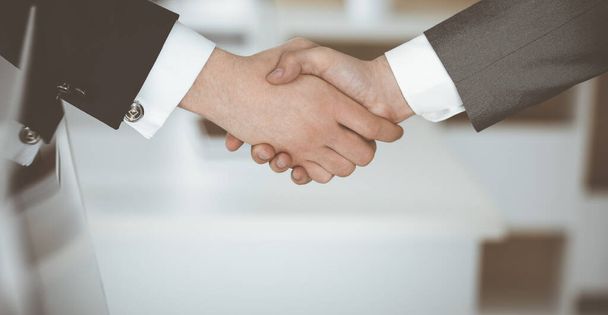 Unknown businessman shaking hands with his colleague or partner while standing straight in modern office, close-up. Business people group at meeting - 写真・画像