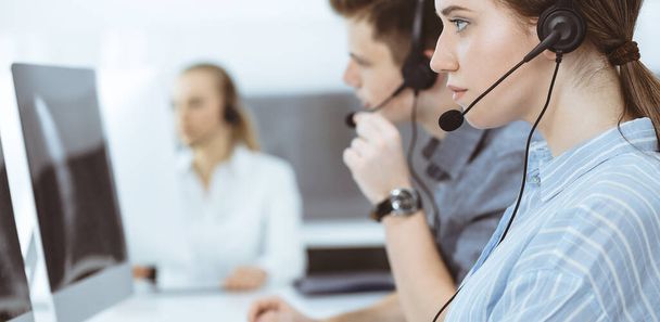 Call center. Group of casual dressed operators at work. Brunette business woman in headset at customer service office - Photo, image