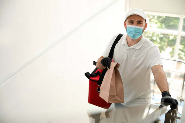 Courier in protective mask and gloves with order indoors. Restaurant delivery service during coronavirus quarantine - Photo, Image