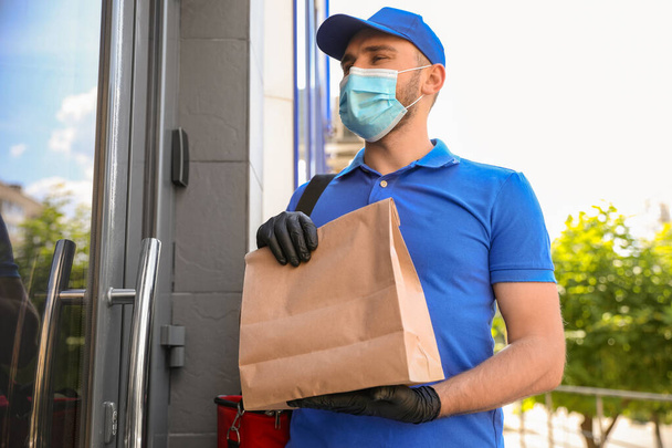 Courier in protective mask and gloves with order near front door. Restaurant delivery service during coronavirus quarantine - Foto, imagen