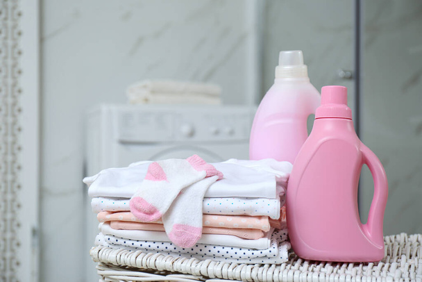 Bottles of detergent and children's clothes on wicker basket in bathroom - Фото, зображення