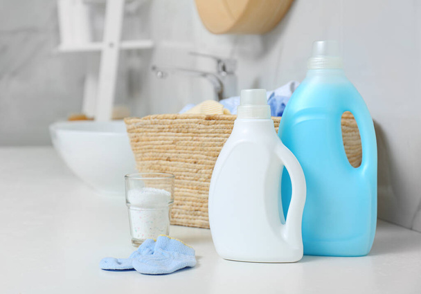Bottles of detergent and children's clothes on countertop in bathroom - Foto, Imagen