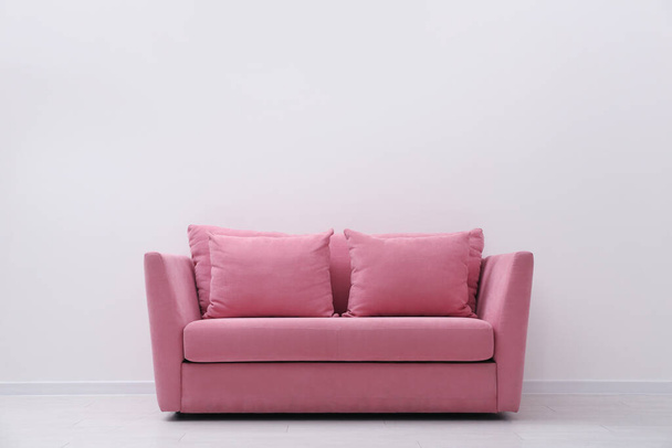 Comfortable pink sofa near white wall indoors, space for text. Simple interior - Zdjęcie, obraz