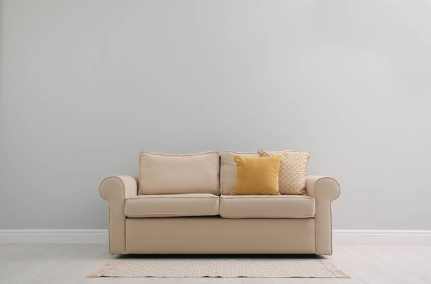 Comfortable beige sofa near light wall indoors, space for text. Simple interior - Фото, зображення