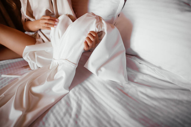 woman examines white dress of bride sitting on bed - Foto, imagen
