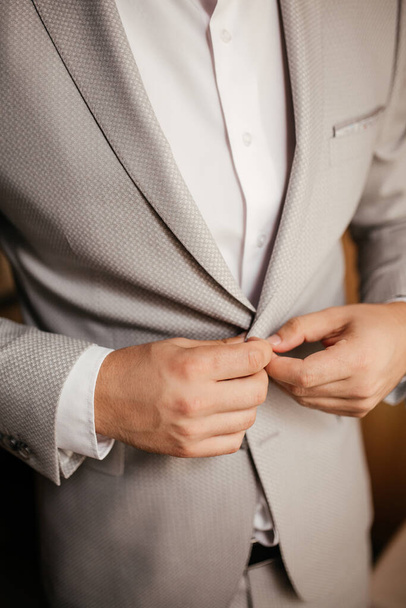 The groom buttons his jacket in room - Fotografie, Obrázek