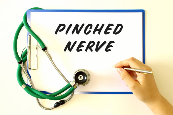 Arzt macht die Aufschrift PINCHED NERVE in das Dokument. Ordner und Stethoskop auf weißem Hintergrund. Medizinisches Konzept. - Foto, Bild