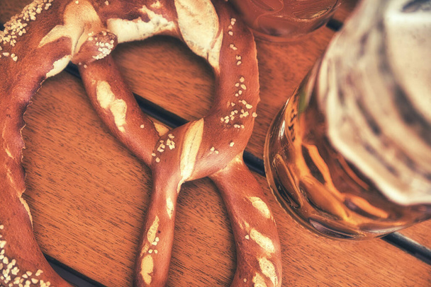 Szklanka piwa piwnego z tradycyjnymi solonymi precelkami na drewnianym tle. Widok z góry, Tradycyjne niemieckie jedzenie - Zdjęcie, obraz