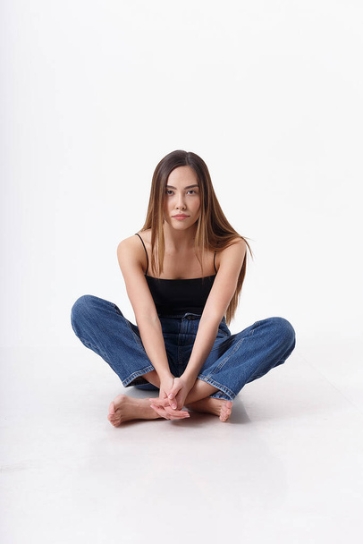 young attractive asian woman with long hair in black top, blue jeans on white - Fotoğraf, Görsel