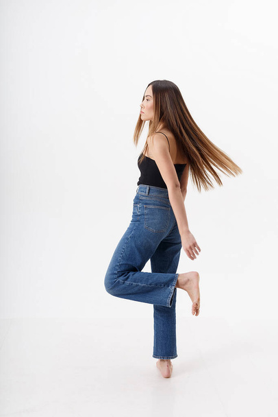 young attractive asian woman with long hair in black top, blue jeans on white - Zdjęcie, obraz
