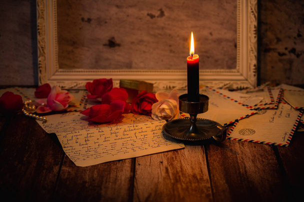 Sobres con letras románticas dentro de ellos iluminados por una vela sobre fondo de madera con marco de foto vacío en el fondo - Foto, imagen