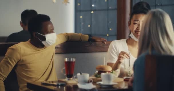 Czarny mężczyzna w masce rozmawia z wielonarodowymi kobietami w kawiarni - Materiał filmowy, wideo