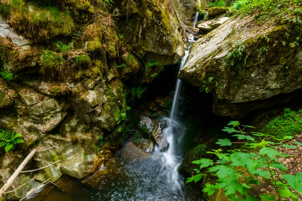 petite cascade entre de gros rochers dans une gorge lors d'une randonnée au printemps - Photo, image