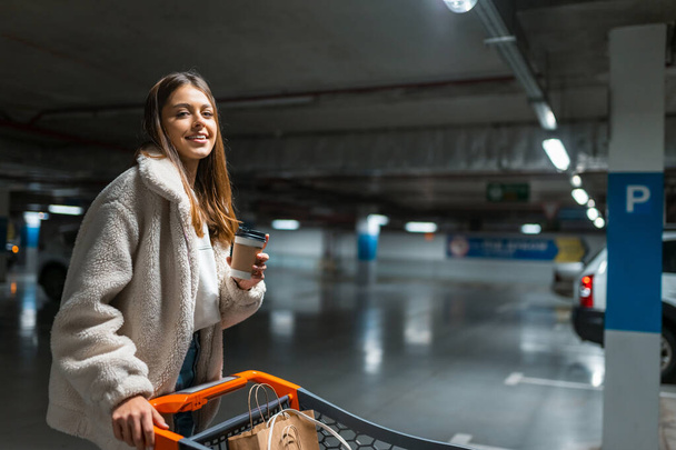 Alışveriş merkezinin yeraltı otoparkında elinde kahve ve tramvayla güzel bir kız. - Fotoğraf, Görsel