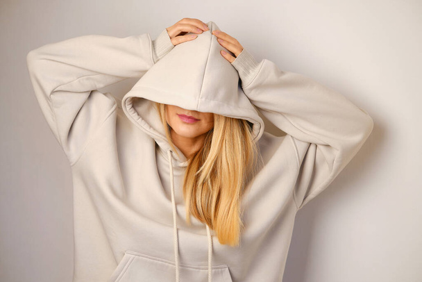 Young beautiful girl in a white hoodie posing. Warm oversized hoodie with an hood. Stylish trendy hipster bow. Trying on clothes in a store. Youth subculture. Fashion clothing advertising - Foto, afbeelding