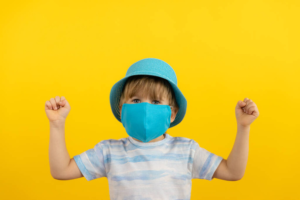 Happy child dreaming about vacation. Portrait of kid wearing protective mask indoor. Summer holiday during coronavirus COVID-19 pandemic concept. - Photo, Image