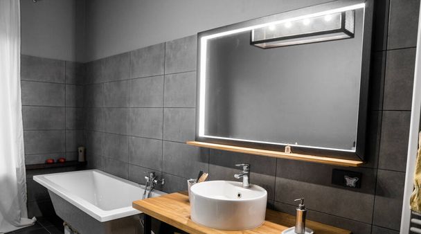 Bathroom in a concrete style with a bath, sink and big mirror. - Fotó, kép