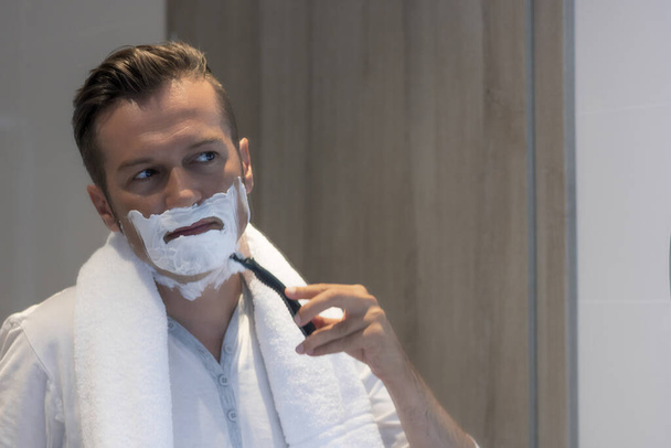 Отражение в зеркале мужчины, бреющегося в ванной. - Фото, изображение