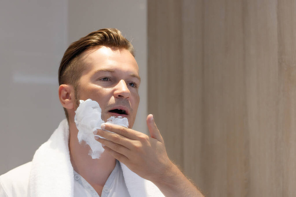 Αντανάκλαση στον καθρέφτη ενός άνδρα που χρησιμοποιεί κρέμα ξυρίσματος στο μπάνιο.  - Φωτογραφία, εικόνα