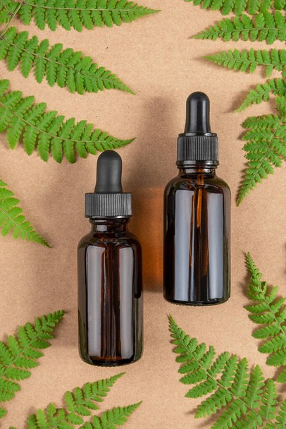 Two brown glass bottles with serum, essential oil or other cosmetic product and green fern leaves on craft beige background. Natural Organic Spa Cosmetic Beauty concept Top view. - Foto, Bild