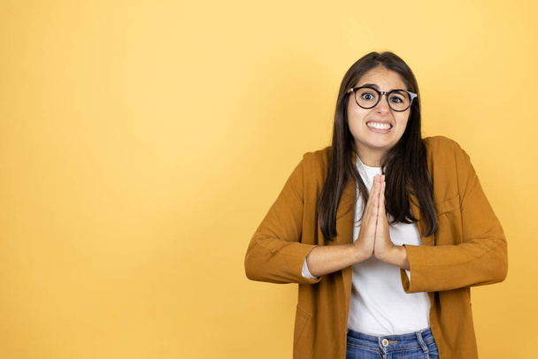 Young beautiful woman wearing a blazer over isolated yellow background begging and praying with hands together with hope expression on face very emotional and worried - Photo, Image