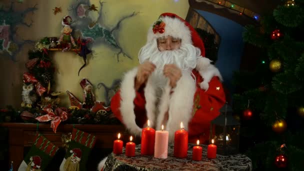 Jolly Santa Claus preens, recht zijn kleren, streelt zijn baard in de buurt van de kerstboom. - Video